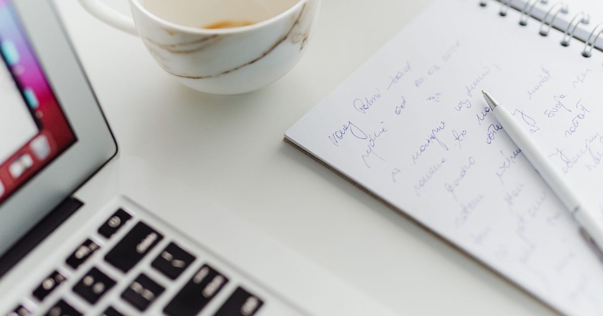 Pisanie na laptopie przy kuchennym stole z notatnikiem - blog firmowy małej firmy w UK